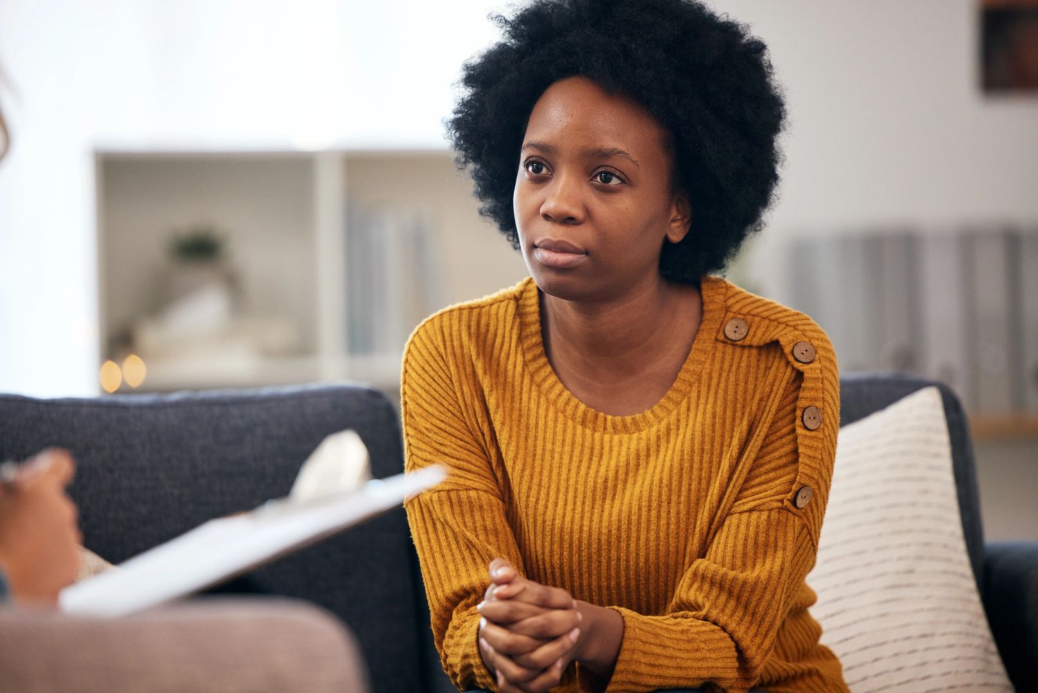 A woman in a mustard sweater attentively listens during a therapy session.