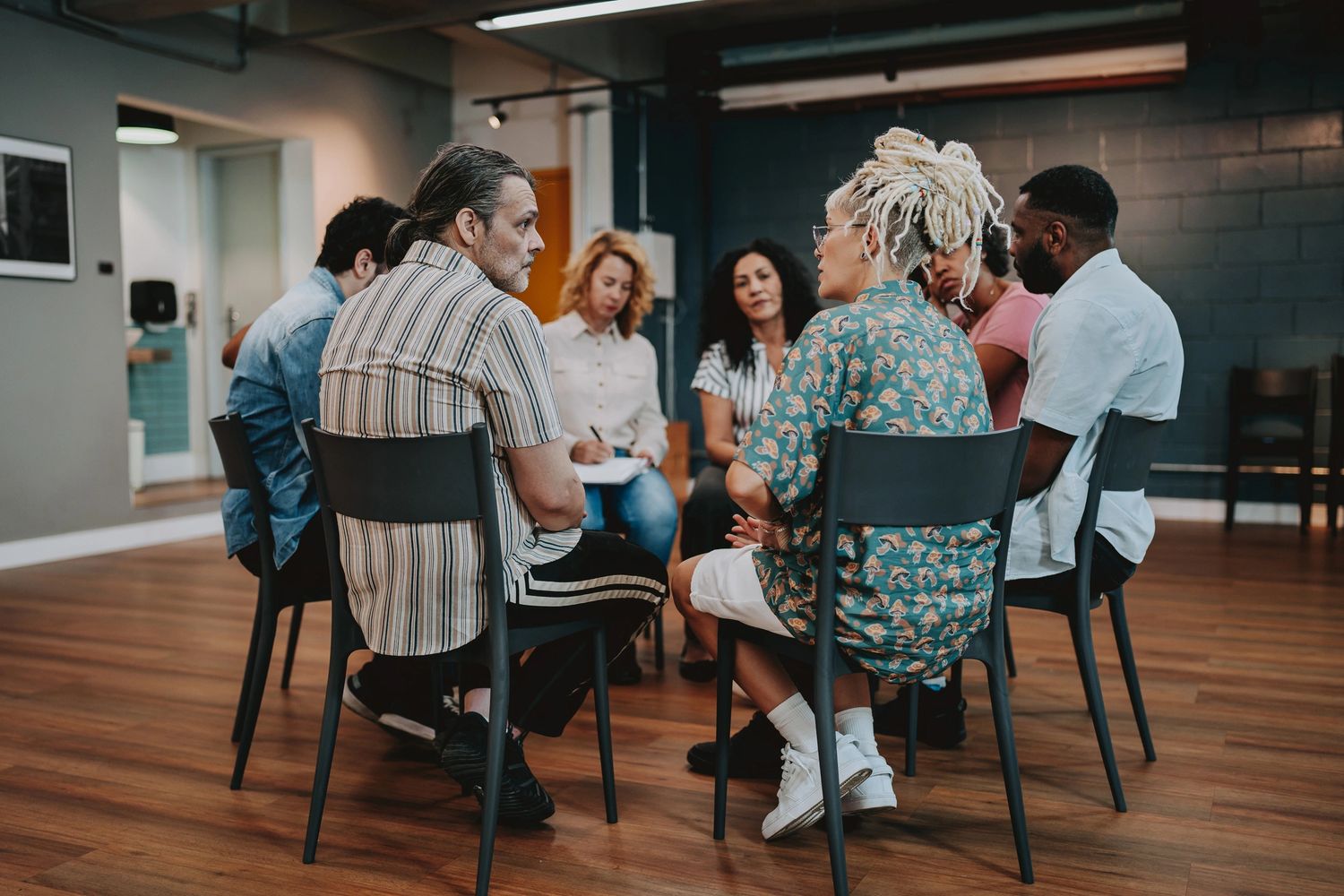 People sitting in a circle engaged in a group discussion in a casual indoor setting.