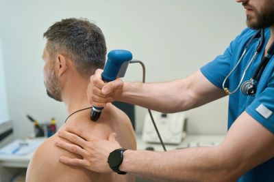 Therapist treating man with shockwave therapy on shoulder.