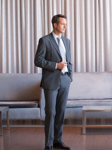 Businessman in suit contemplating white stacked cubes on table in modern office.
