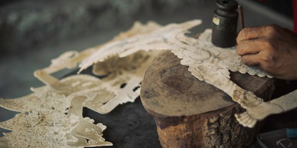 Handcrafting an intricate shadow puppet from leather with detailed patterns.