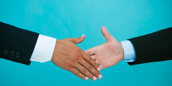 Two people in suits reaching for a handshake against a blue background.