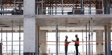 Two construction workers discussing plans inside a building under construction. Commercial concrete services. Concrete foundations. Residential concrete projects.