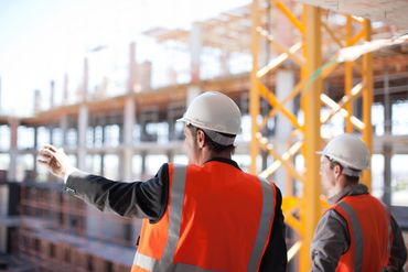 Two construction workers in hard hats and safety vests inspecting site.
