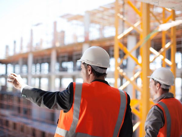 Two construction workers in safety gear discussing a building site.