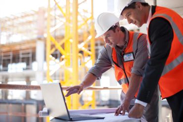 Engineers reviewing plans on a laptop at a construction site.