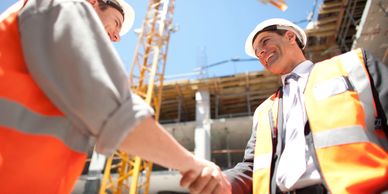 Two construction workers in safety gear shaking hands at a building site.