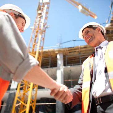 Two construction workers shaking hands at a building site.