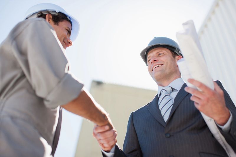 Businessman with blueprints shaking hands with worker