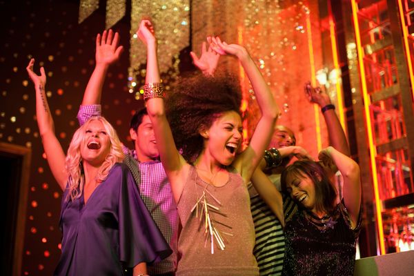 Group of friends joyfully dancing with hands raised in a vibrant club setting.