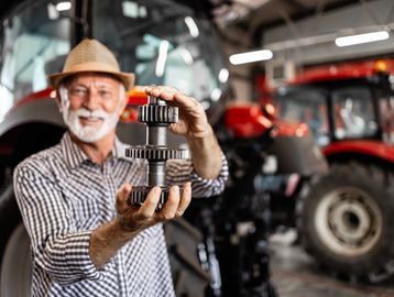 Smiling farmer holding a tractor gear in a workshop.