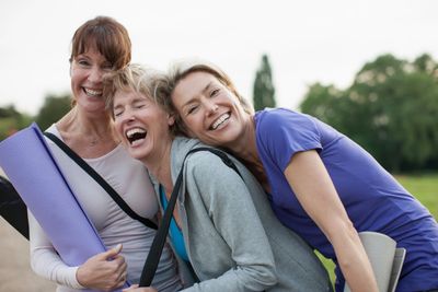 Three women smiling and holding yoga mats outdoors.