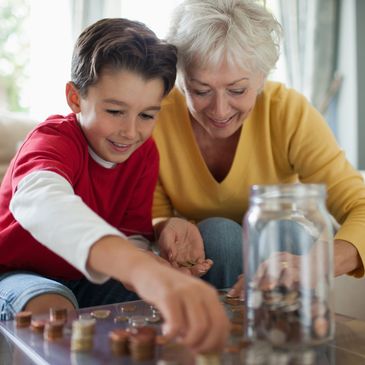 A boy and an elderly woman happily counting coins together at home.