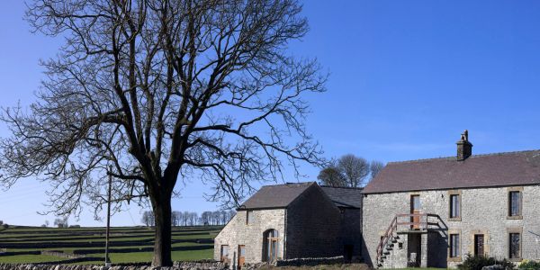Stone-built farmhouse under a clear blue sky with a large leafless tree.