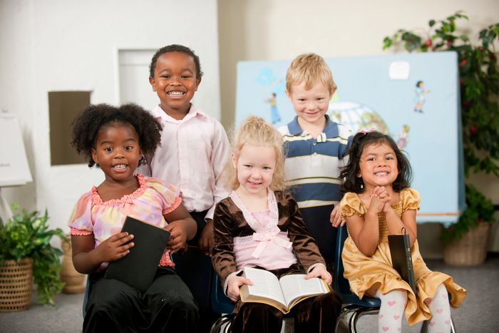 Five diverse children smiling and holding books in a classroom setting.