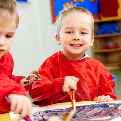 Two children in red smocks enjoying finger painting.