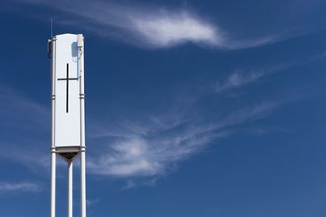 White modern water tower with a cross under blue sky.
