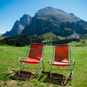 Two red chairs on green grass with a mountain backdrop under a clear blue sky.