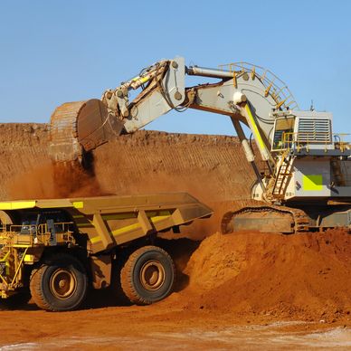 Excavator loading dirt into a large mining truck in an open-pit mine.