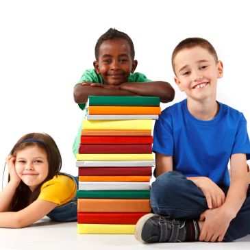 Three children sitting with a tall stack of books.
