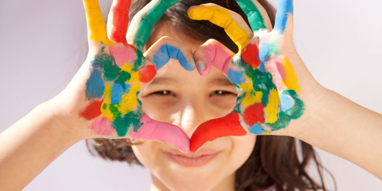Child with colorful painted hands making a heart shape.