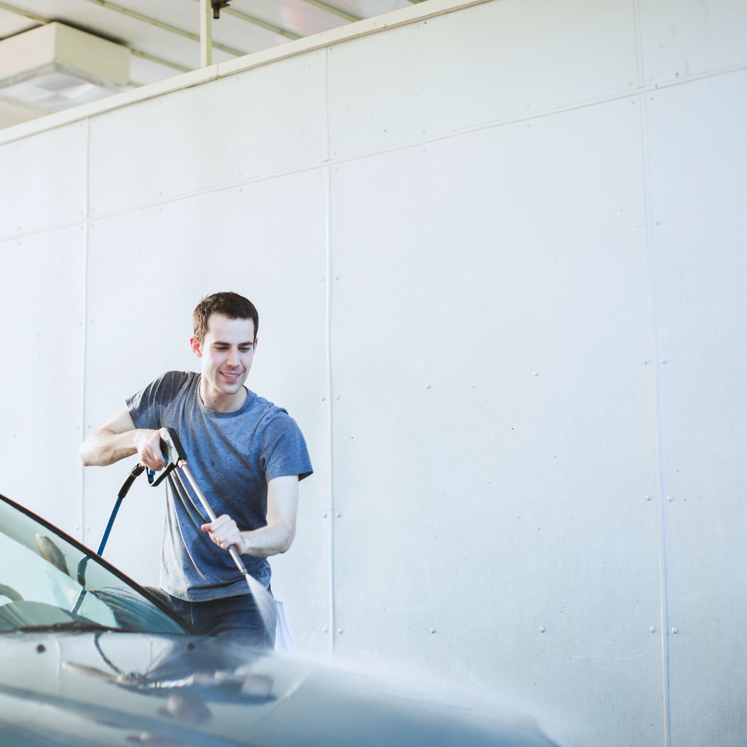 A man washing a car with a pressure washer outdoors.