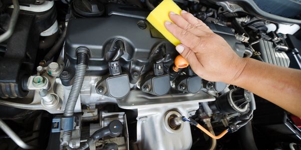 Hand cleaning a car engine with a sponge.