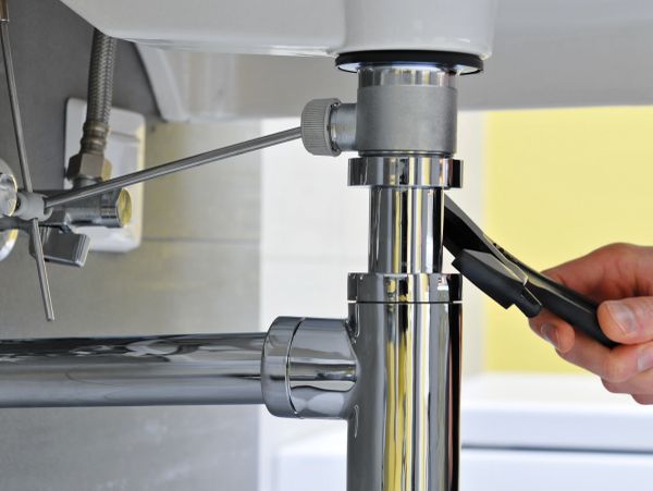 Hand using pliers to fix a chrome pipe under a sink.
