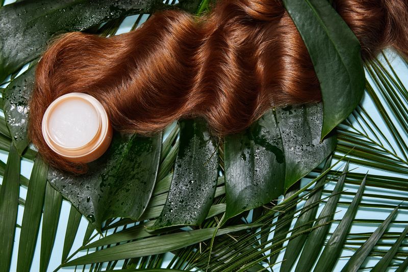 Photo of long wavy brunette hair and hair treatment mask against beige background and floral elements. top view, flat lay. copy space. Self care. Natural beauty, organic, hair care product concept.