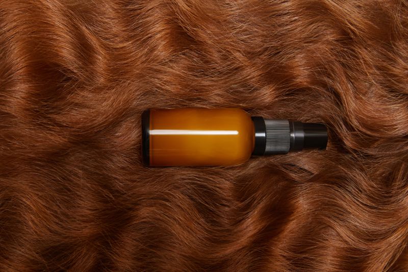 Photo of bottle pray in wavy silky shiny long brunette hair. top view, flat lay. copy space. Self care, hair treatment. Natural beauty, organic cosmetic, hair care products, spa concept. ad