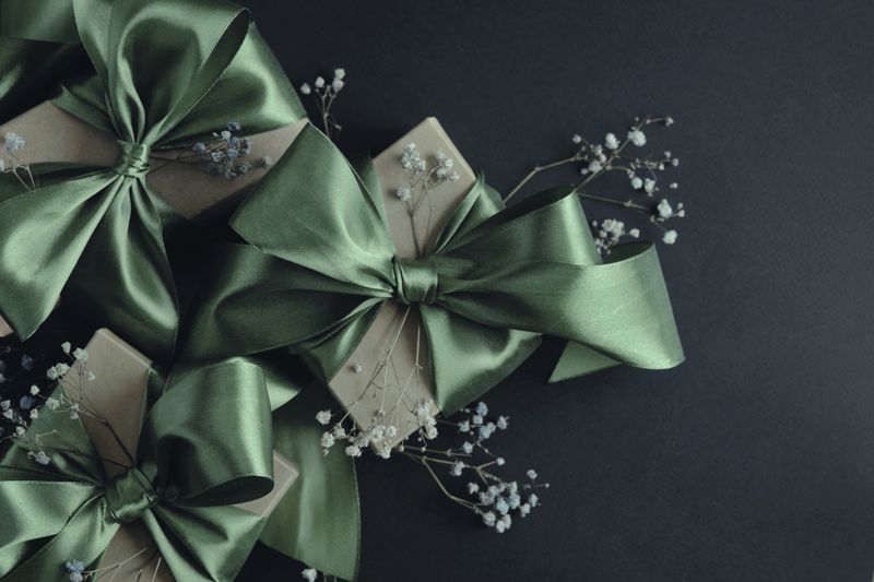 Gift boxes with olive green ribbons tied in a bow. Black background, top view. Decoration for holidays, birthdays, weddings.