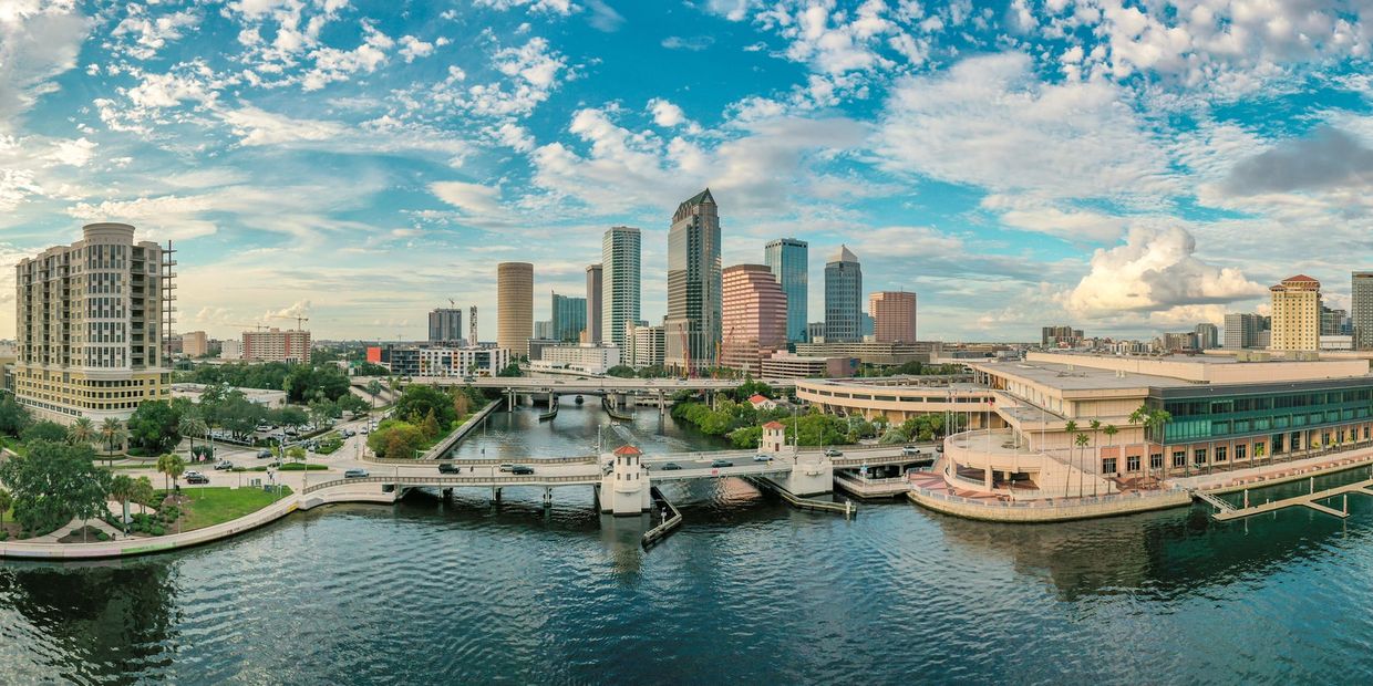 Panoramic view of a city skyline with a waterfront and bridges under a partly cloudy sky.