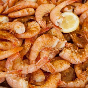 A close-up of cooked shrimp seasoned with spices and a lemon wedge.