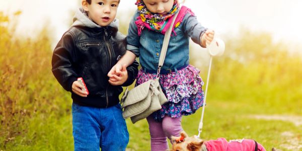Two young children walking a small dog on a grassy path.