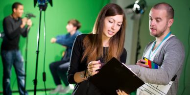 Two people reviewing a clipboard on a film set with a green screen.