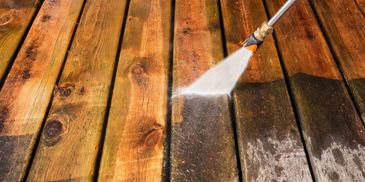 Pressure washing a wooden deck to remove dirt and grime.
