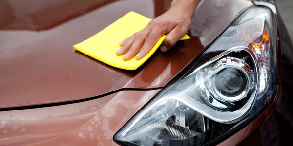 Person polishing a brown car with a yellow cloth.