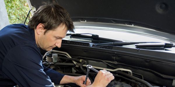 A mechanic working on a car engine with a wrench under the hood.