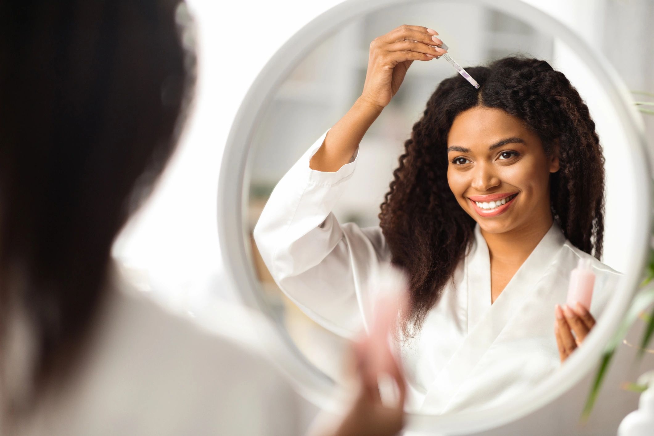 Woman applying hair serum in front of mirror.
