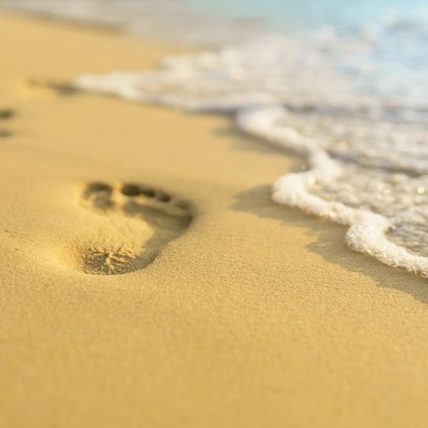 Footprint on sandy beach near gentle ocean waves.