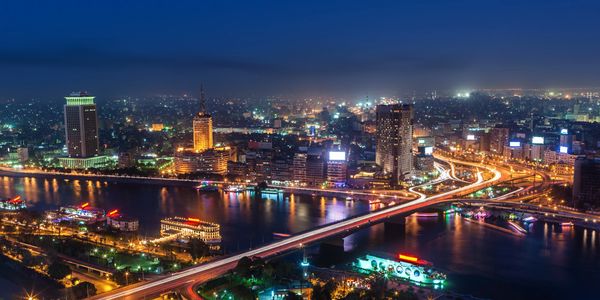 Nighttime cityscape with illuminated bridge over a river.