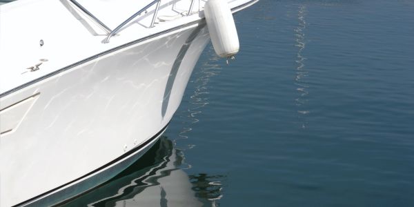 Close-up of a white boat's bow with a fender hanging over calm water.