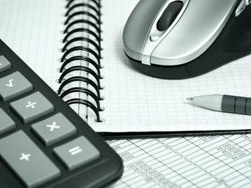 Calculator, notebook, pen, and mouse on a desk with financial data.