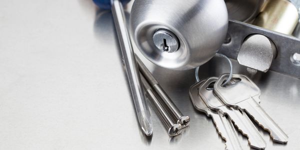 Close-up of door lock, keys, and screwdrivers on a metal surface.