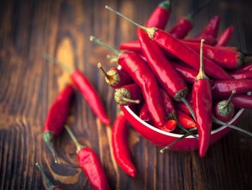 A bowl full of red chili peppers on a wooden surface.