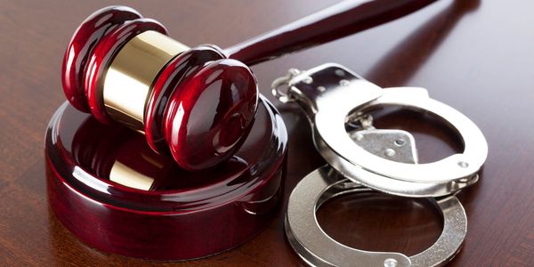 A judge's gavel and a pair of handcuffs on a wooden surface.