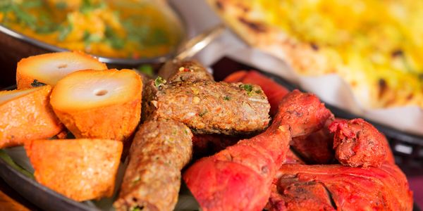 A plate of mixed Indian grilled meats and vegetables with naan bread in the background.