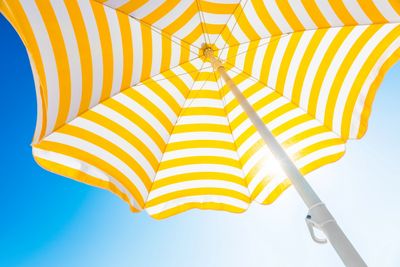 Yellow and white striped umbrella against blue sky.