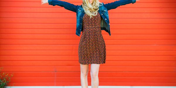 Woman spreading arms wide, smiling in front of a vibrant red wall.