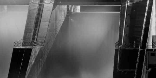 Black and white photo of a dam under construction in a rocky canyon.